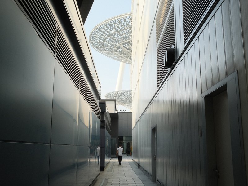 A narrow alleyway between modern buildings leading to a large structure above.