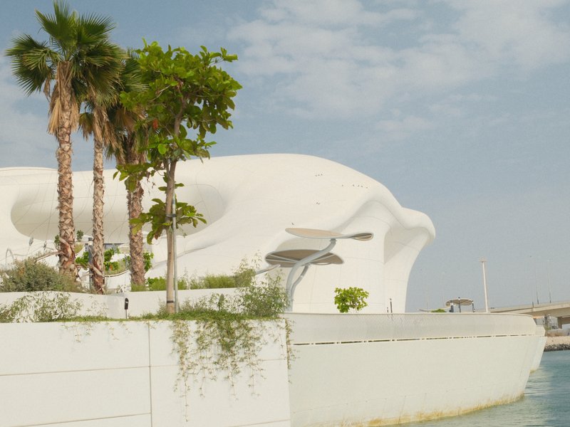 Modern architectural structure with palm trees against a clear sky near water.