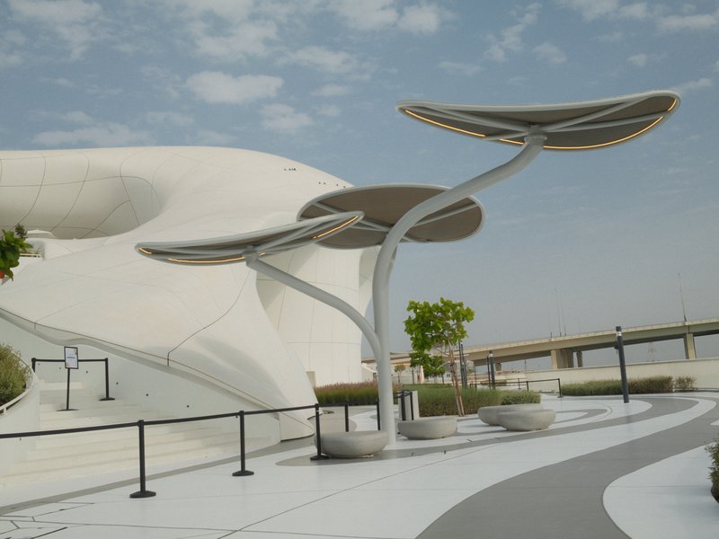 Modern architectural structure with curved canopies and greenery against a cloudy sky.