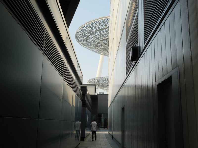 Narrow urban alleyway leading to a modern architectural structure with a large canopy overhead.
