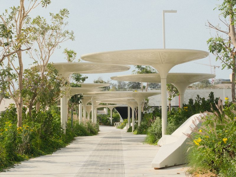 A modern pathway lined with unique architectural canopies and greenery on both sides.