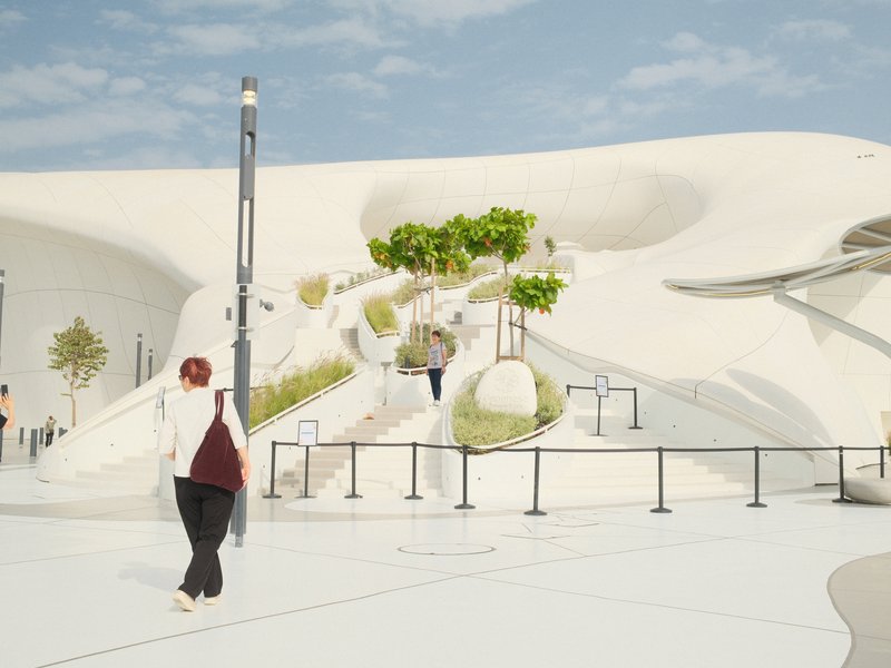 A person walking towards a modern architectural structure with white curves and greenery.