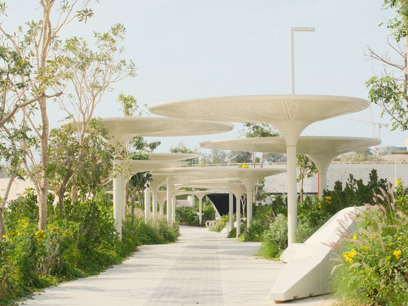 A modern pathway lined with unique umbrella-like structures and greenery on both sides.