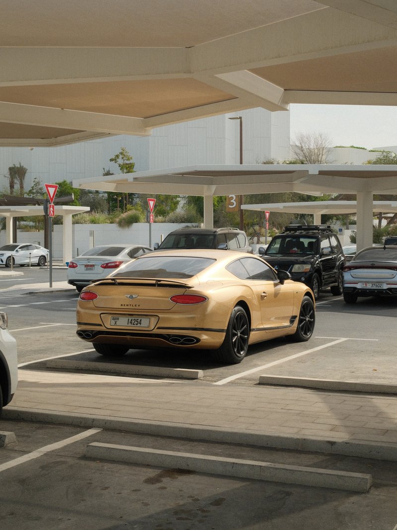 A gold luxury car parked in a modern parking structure with other vehicles in view.