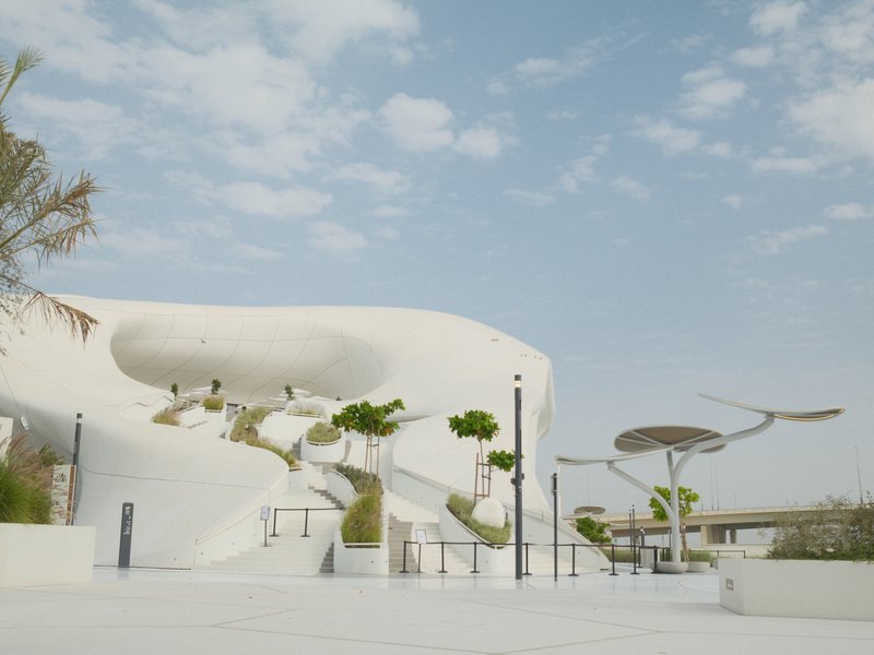Modern architectural structure with white curves and greenery under a partly cloudy sky.