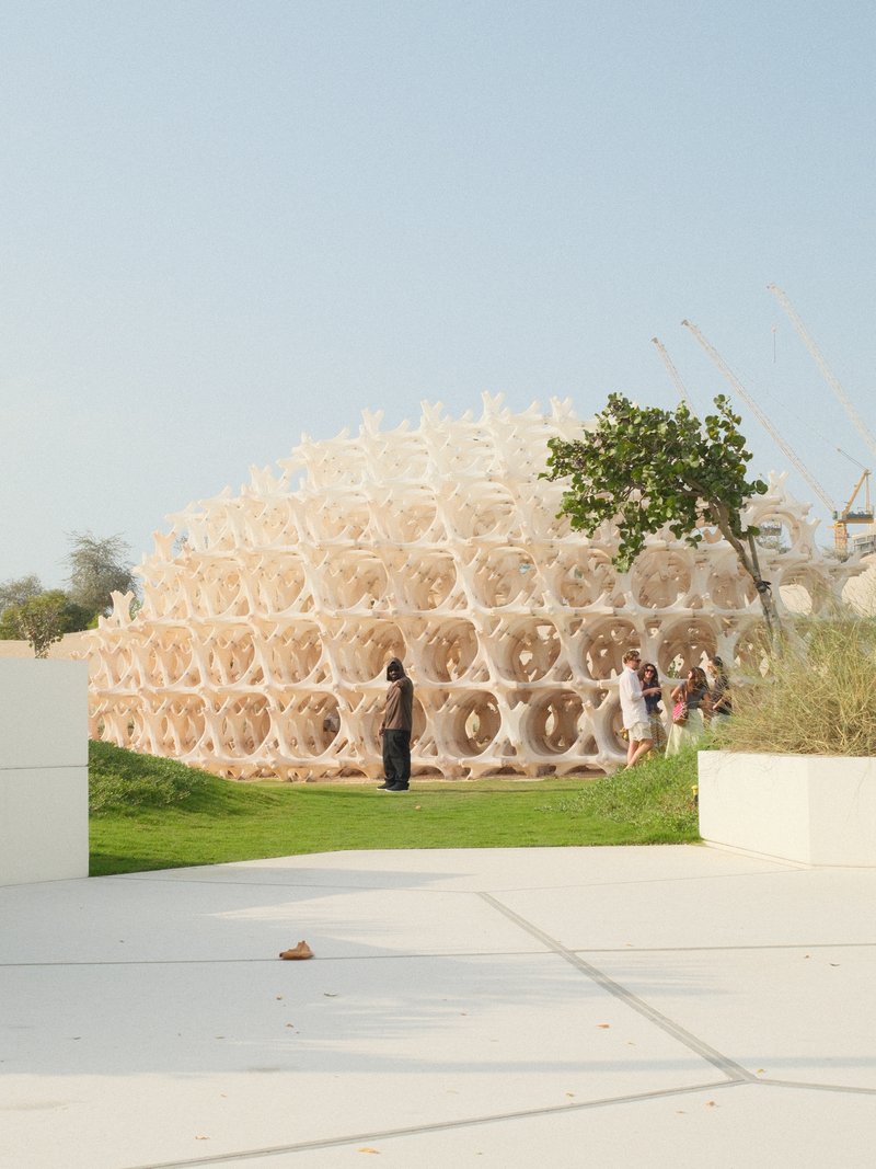 A unique architectural structure resembling a honeycomb, with people interacting around it in a sunny outdoor setting.