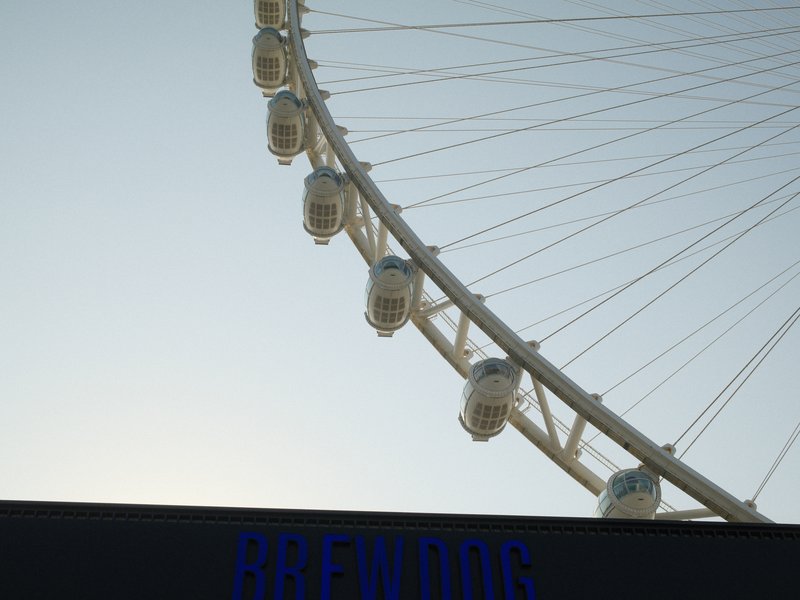 Close-up of a ferris wheel against a clear sky, with a sign partially visible at the bottom.