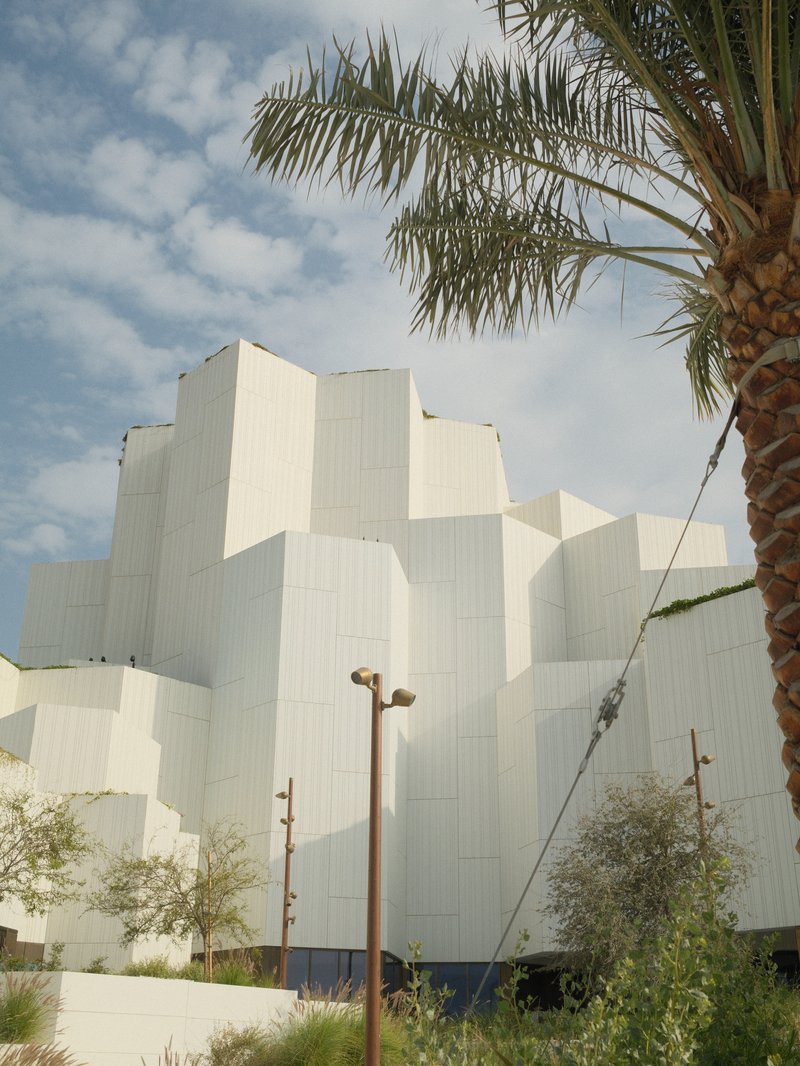Modern architectural building with white geometric shapes against a cloudy sky and palm tree.