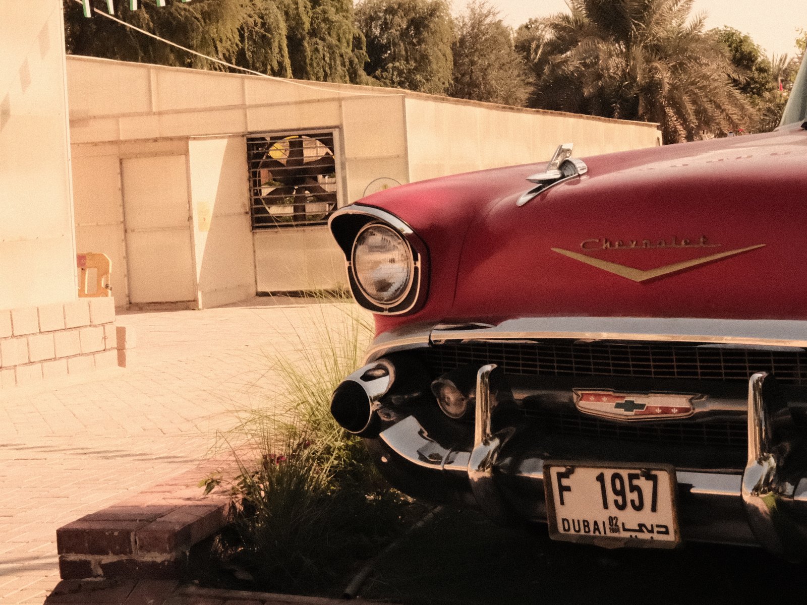 Close-up of a vintage red car parked near a building with palm trees in the background.
