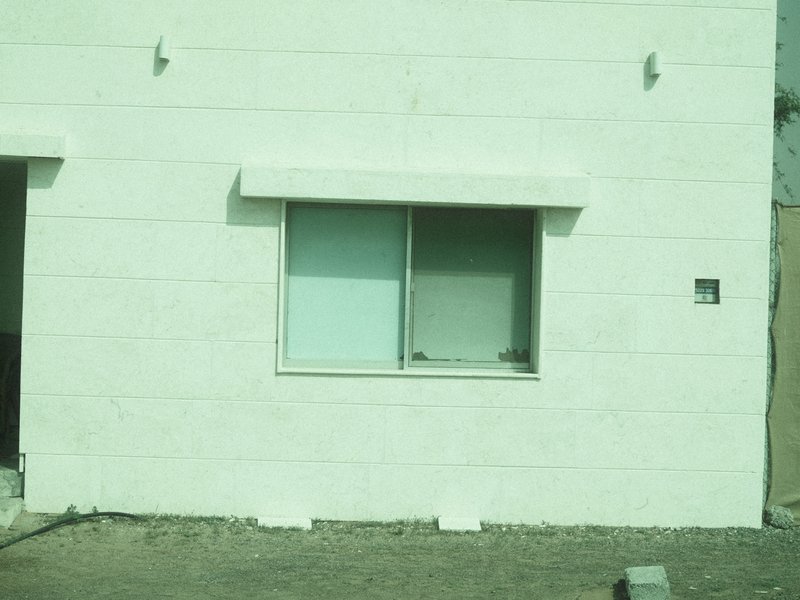 A simple white building with a single window, featuring a light green tint.