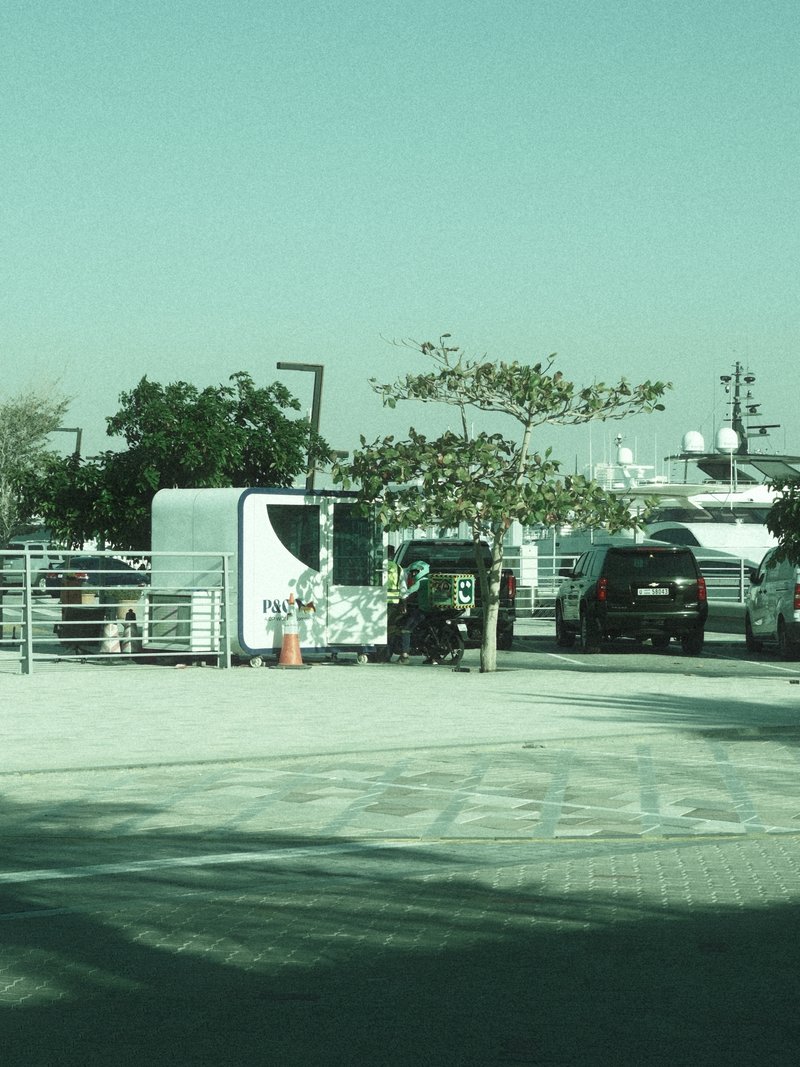 A parking area with cars, trees, and a white structure under a clear sky.