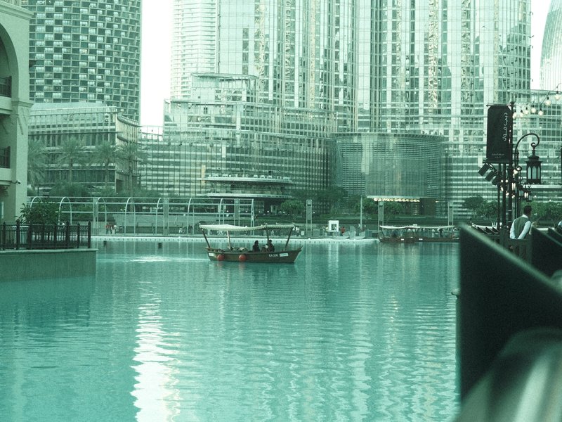 A serene view of a turquoise lake surrounded by modern skyscrapers with a small boat in the water.