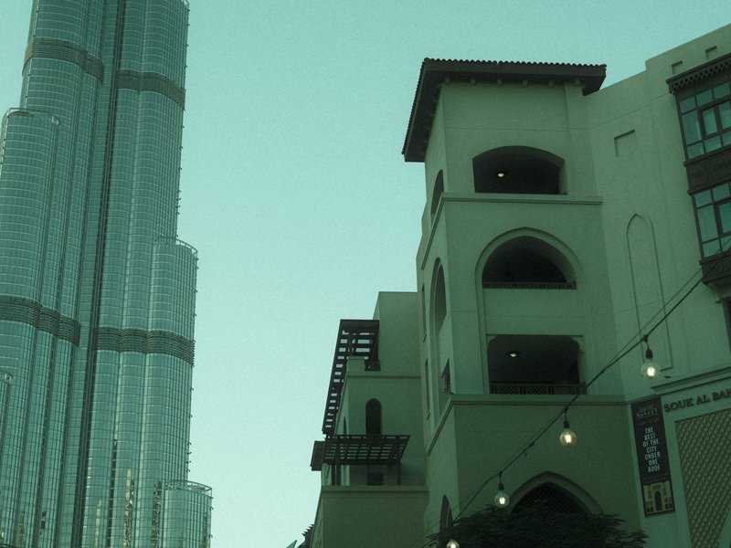 A tall modern skyscraper next to a traditional-style building under a clear sky.