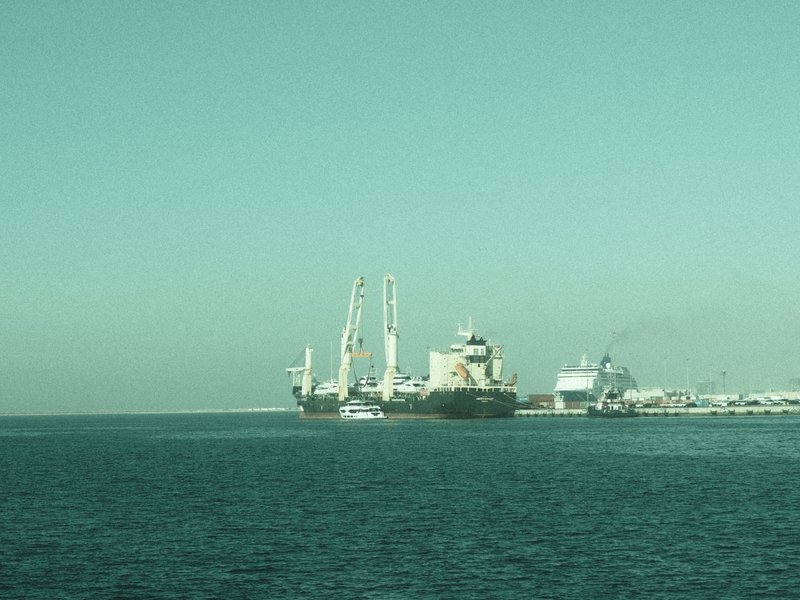 A view of large ships docked at a port with calm waters and a clear sky.