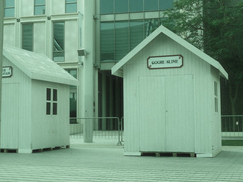Two small white wooden houses in an urban setting with a modern building in the background.