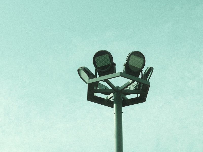 A tall light pole with multiple floodlights against a pale sky.