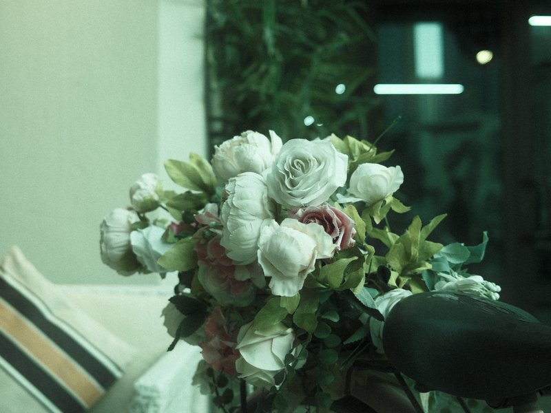 A close-up of a bouquet of artificial flowers with soft colors, set against a blurred indoor background.