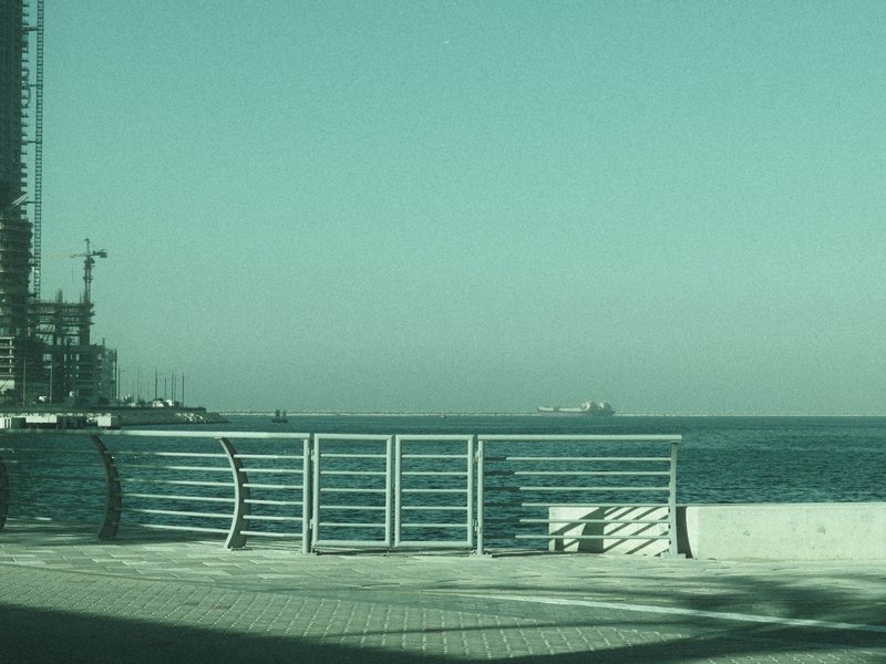 A coastal view featuring a railing, distant ships, and a clear sky.