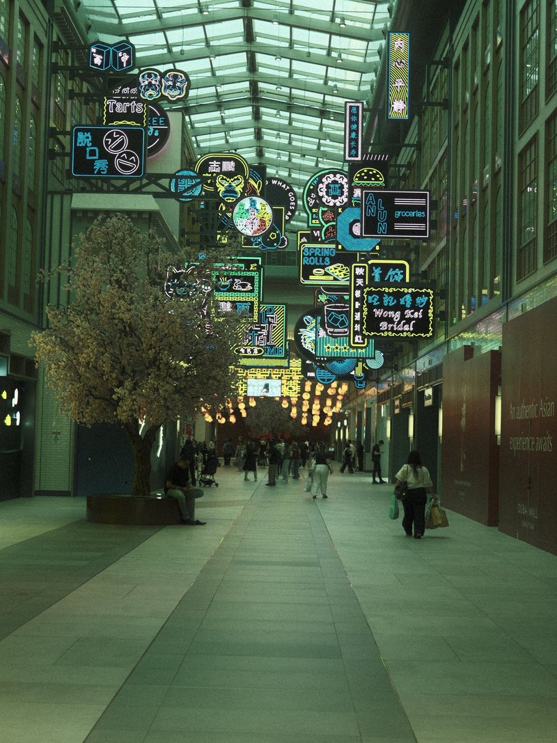 A vibrant indoor shopping arcade with colorful neon signs and a cherry blossom tree.