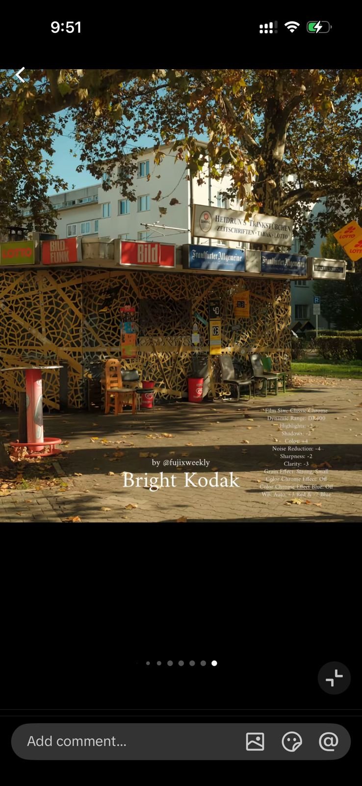 A vibrant street scene featuring a small vendor stall surrounded by trees and urban buildings.