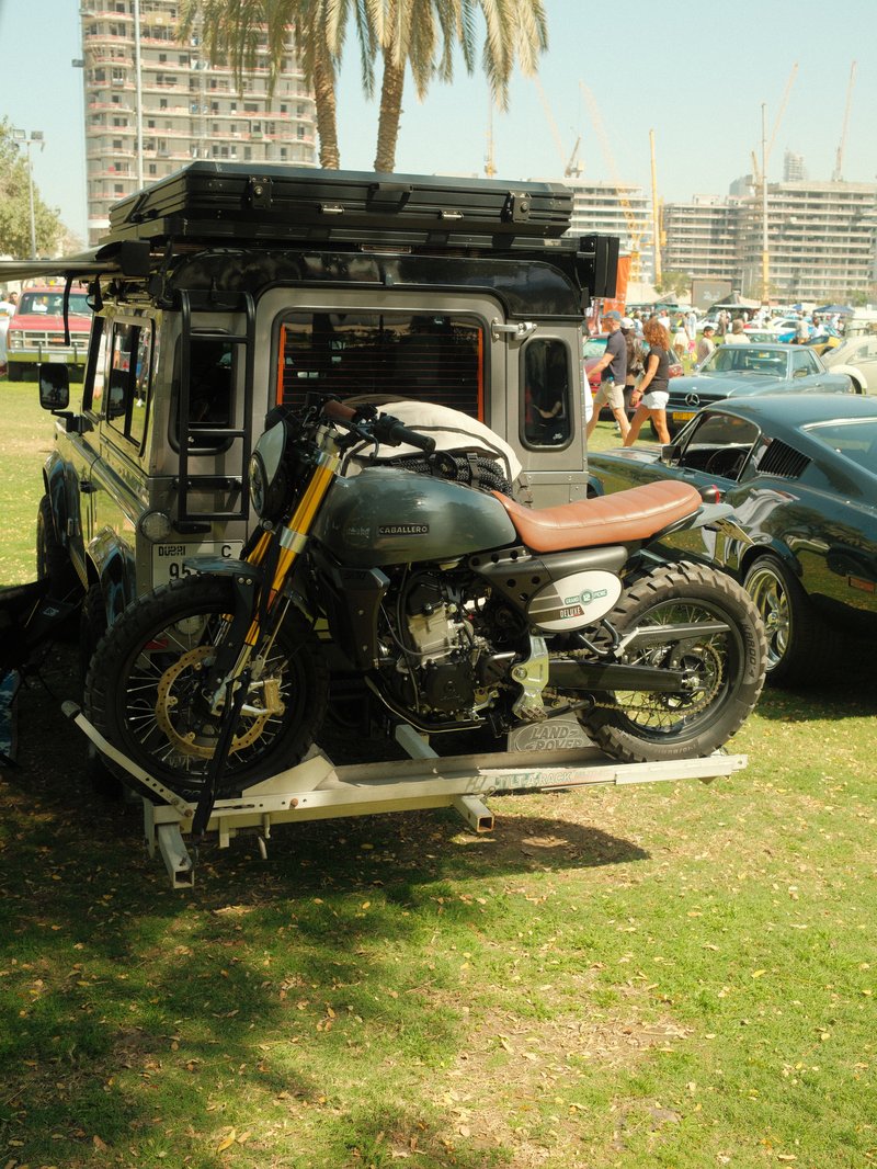 A motorcycle mounted on a trailer attached to a vehicle in a sunny outdoor setting with palm trees.