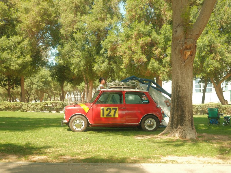 A red vintage car with the number 127 parked under a tree in a grassy area.