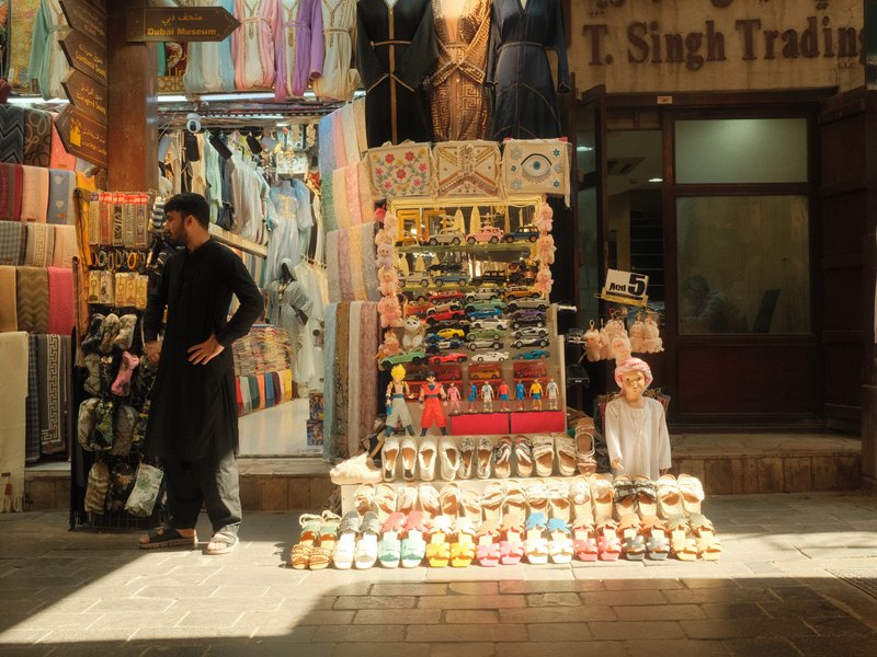 A vibrant street market scene with a vendor and colorful merchandise displayed in a narrow alley.