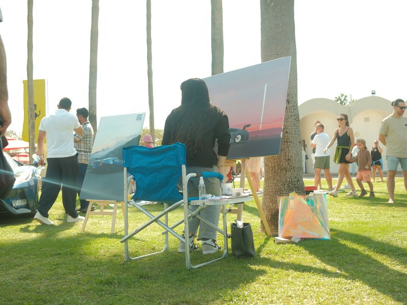 An artist painting outdoors with a canvas, surrounded by people at a vibrant event.