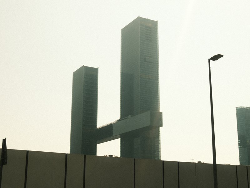 Two tall modern buildings connected by a horizontal structure, shrouded in a hazy atmosphere.