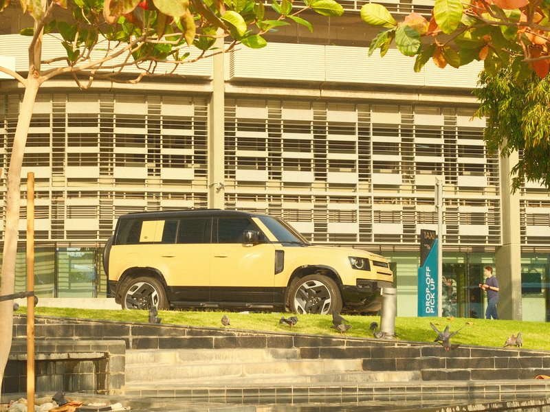 A yellow SUV parked on a grassy area near a modern building with large windows.