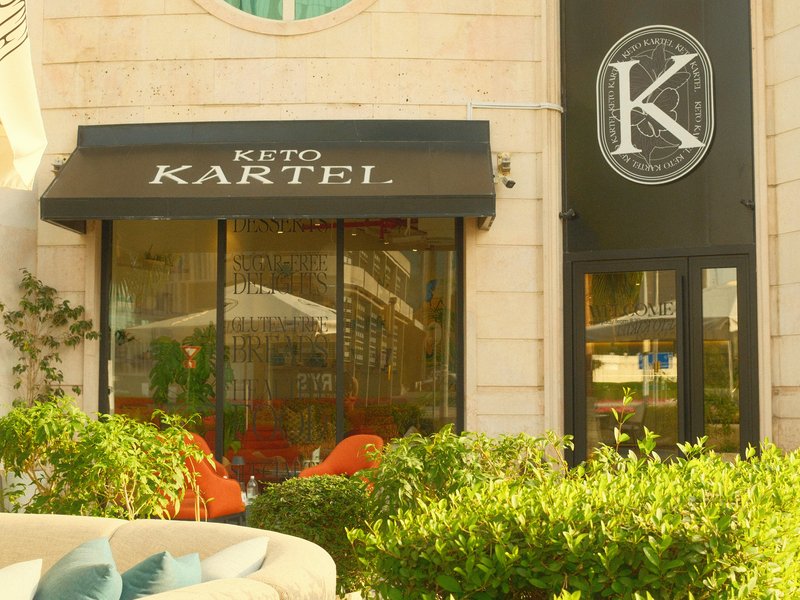 Exterior view of a restaurant named Keto Kartel with outdoor seating and greenery.