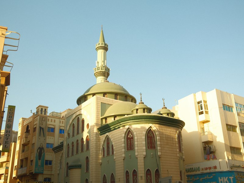 A green and cream mosque with a tall minaret against a clear blue sky.
