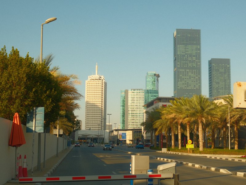 View of a modern urban street with tall buildings and palm trees under a clear blue sky.
