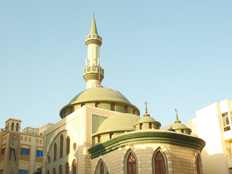 A mosque with a green dome and minaret against a clear blue sky.