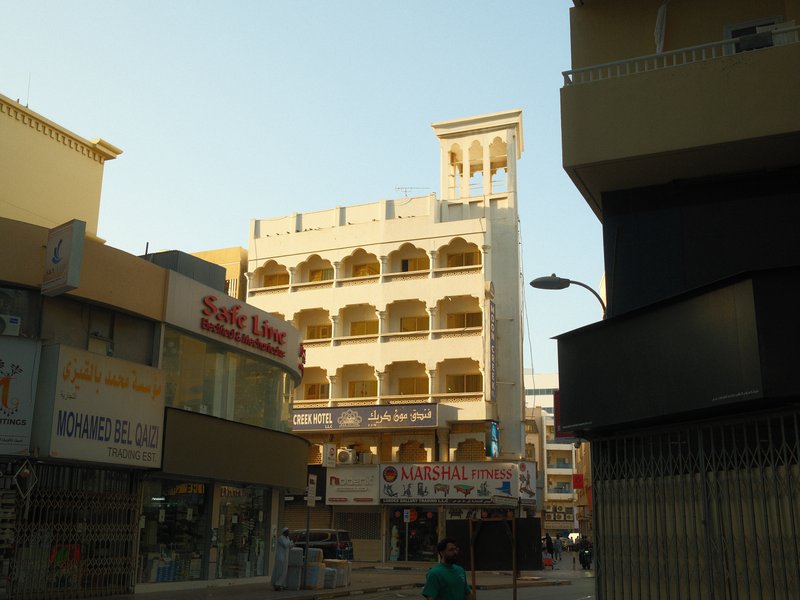 A street view featuring a traditional building with arches and a tower, surrounded by modern shops.
