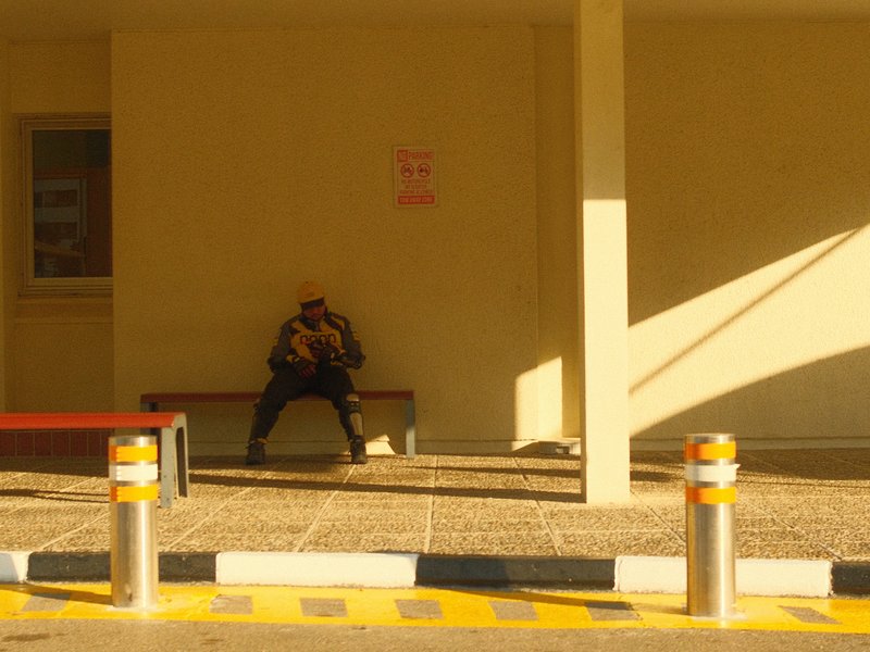 A person sitting on a bench in a minimalist setting with warm light casting shadows.