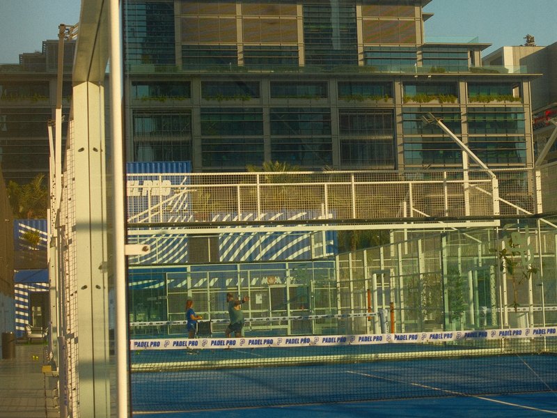 Reflection of modern buildings on glass walls of a sports facility with blue court.