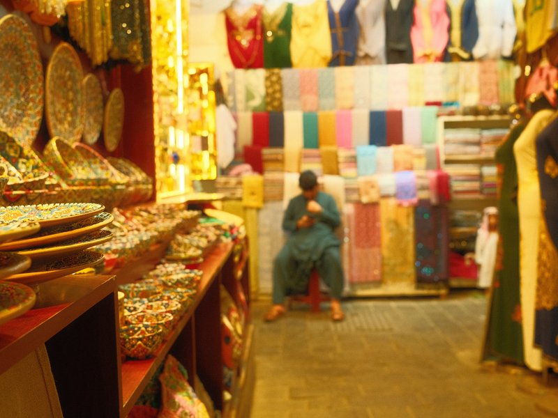 A vibrant textile shop with colorful fabrics and decorative items, featuring a person sitting quietly.