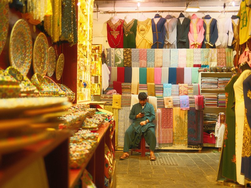 A person sitting in a vibrant textile shop surrounded by colorful fabrics and decorative items.