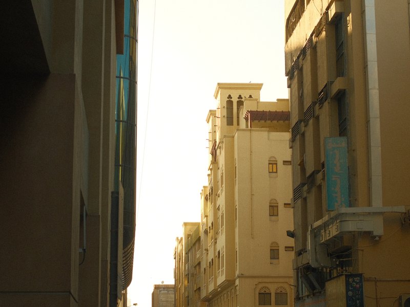 Narrow urban alley with tall buildings and a warm golden light illuminating the scene.