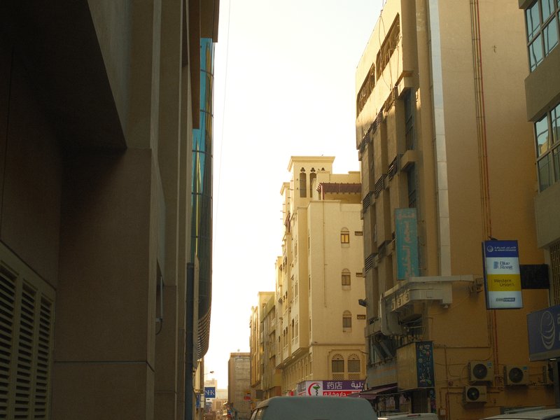 Narrow urban alleyway with tall buildings on either side and a clear sky above.