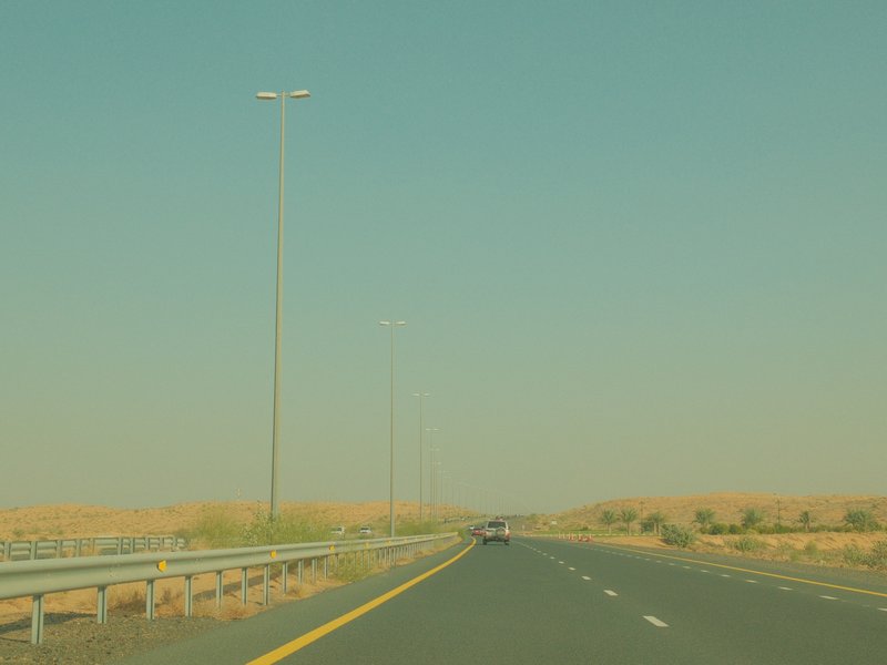 A long, empty highway stretching into the distance with tall streetlights and desert landscape on either side.