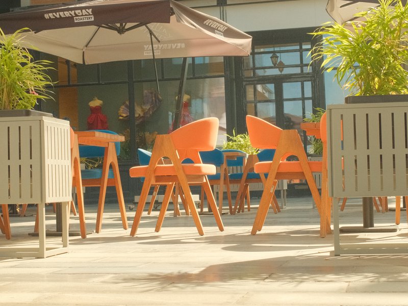 A sunny outdoor café scene with orange chairs and green plants, creating a vibrant atmosphere.