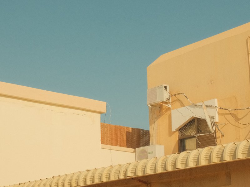 A view of beige buildings with air conditioning units against a clear blue sky.