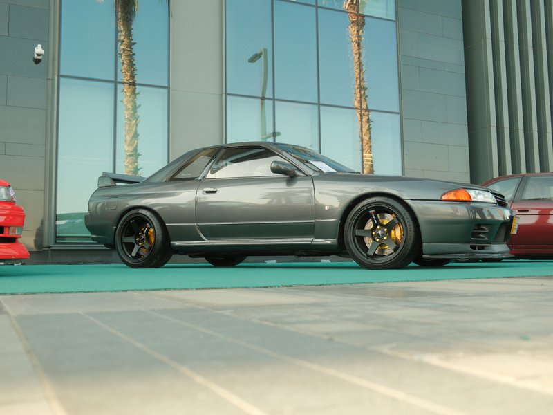 A sleek gray sports car parked on a green surface in front of a modern building with palm trees.