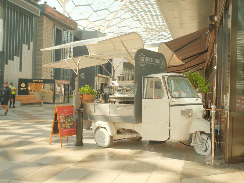 A white food truck with an awning parked indoors in a modern shopping area.