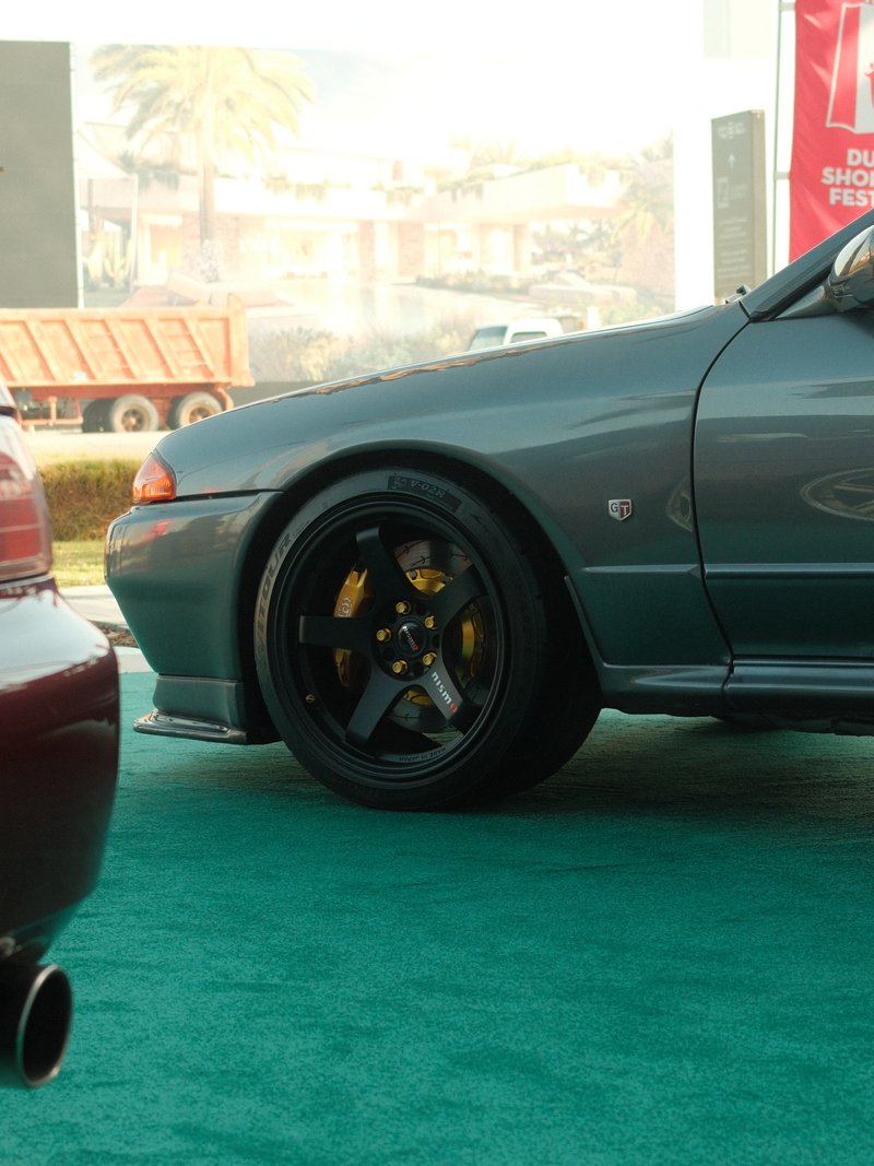 Close-up of a car's wheel and part of the body, showcasing sleek design and shiny rims.