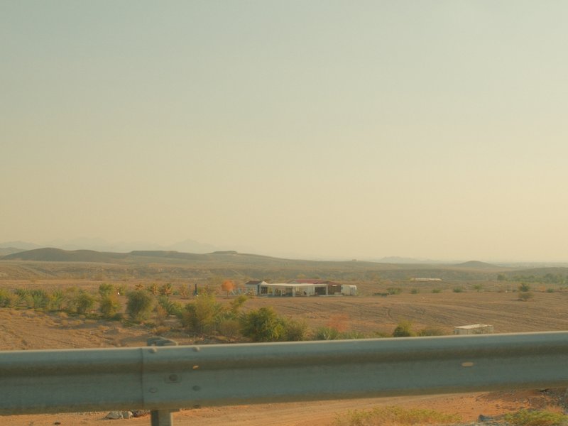 Distant view of a rural landscape with a highway guardrail in the foreground and mountains in the background.