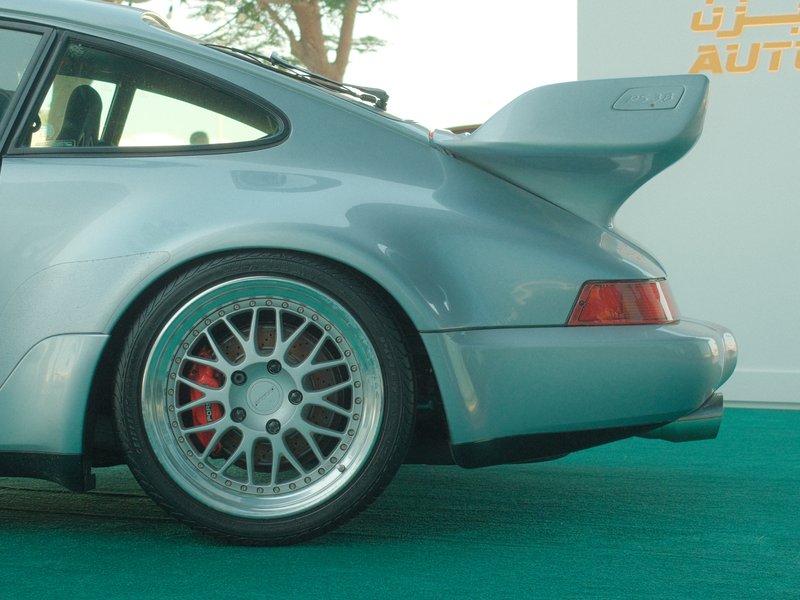 Close-up of a silver sports car with a prominent rear wing and detailed alloy wheels on a green surface.