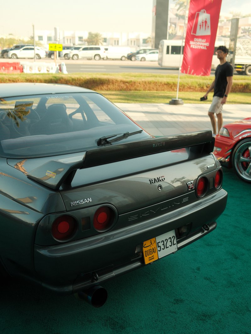 Rear view of a gray Nissan sports car with a large spoiler, parked on green carpet at an outdoor event.